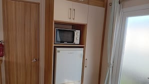 Kompakti keittiö, jossa on valkoinen jääkaappi, mikroaaltouuni ja puiset kaapit.