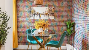 A dining area with a colorful brick wall, a round table, teal chairs, and a hanging light fixture. - Brighton Seaside 1-bed Retreat Near The Lanes (Brighton)