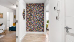 A hallway with a floral-patterned wall, a door with a phone, and a glimpse of a room with a bed and a yellow chair. - Brighton Seaside 1-bed Retreat Near The Lanes (Brighton)