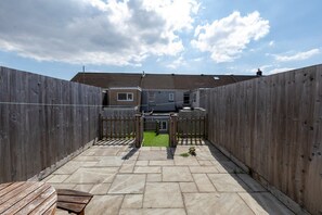 A fenced backyard with a paved patio, a wooden fence, and a house in the background. - Bright 3-bed Swansea House + Parking (Swansea)