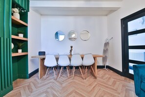 A dining area with a wooden table and white chairs, a green accent wall, and a large window. - Bright 3-bed Swansea House + Parking (Swansea)