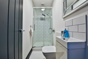 A modern bathroom with a glass-enclosed shower, white tiled walls, a white sink with a blue bottle of hand soap, and a toilet. - Bright 3-bed Swansea House + Parking (Swansea)