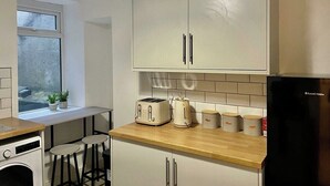 Une cuisine de taille réduite avec des meubles blancs, un plan de travail en bois, un grille-pain, une bouilloire et un réfrigérateur.