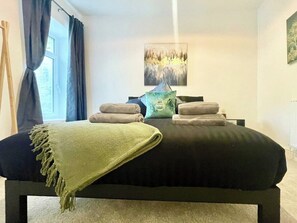 A bedroom with a bed, pillows, a blanket, and a painting on the wall. - Cozy & Spacious 3-bedroom Home (Swansea)
