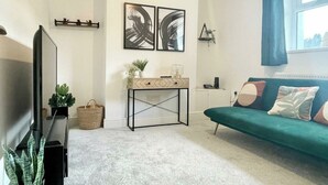 Un salon moderne avec un téléviseur à écran plat, un canapé vert, une table basse et des œuvres d’art abstraites accrochées au mur.