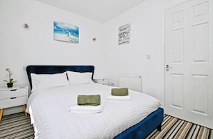 Un dormitorio con cama, paredes blancas, una puerta y un radiador.