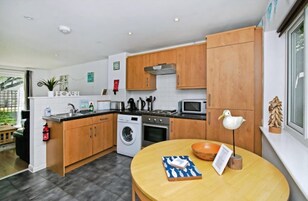 A compact kitchen with wooden cabinets, a washing machine, a microwave, and a dining area with a table and chairs.