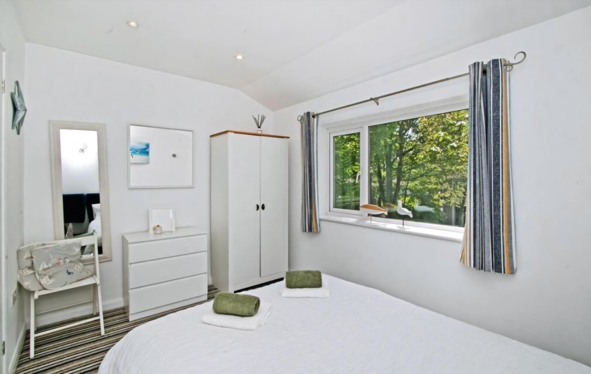A bedroom with a bed, a dresser, a mirror, a window with curtains, and a view of trees.