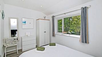 A bedroom with a bed, a dresser, a mirror, a window with curtains, and a view of trees.