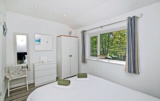 A bedroom with a bed, a dresser, a mirror, a window with curtains, and a view of trees.