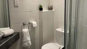 A modern bathroom with a toilet, a glass shower enclosure, a sink with a mirror, and a towel rack. - Atlantic Reach Cosy 2-bed With Parking (St. Columb Major)