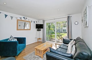 A modern living room with a blue sofa, a black leather sofa, a wooden coffee table, and a TV mounted on the wall. - Atlantic Reach Cosy 2-bed With Parking (St. Columb Major)