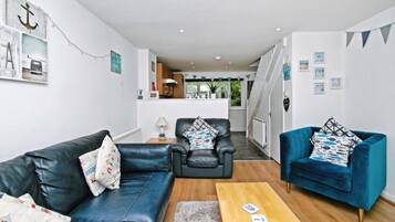 A modern living room with a sofa, two armchairs, a coffee table, and a kitchen in the background.