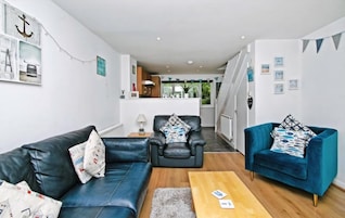 A modern living room with a sofa, two armchairs, a coffee table, and a kitchen in the background.