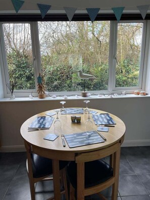 A round wooden table set for four with placemats, wine glasses, and cutlery.