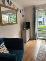 Una sala de estar con un sofá, un televisor sobre un mueble bajo, un espejo y vistas a un patio trasero a través de una puerta corrediza de vidrio.