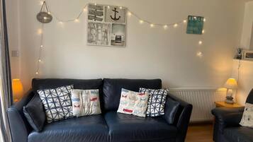 A living room with a black leather sofa, patterned cushions, a wooden coffee table, and string lights.