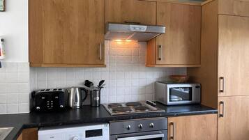 A compact kitchen with wooden cabinets, a built-in washing machine, a microwave, and a gas stove.