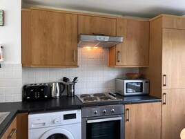 Una cocina compacta con armarios de madera, lavadora integrada, microondas y cocina a gas.