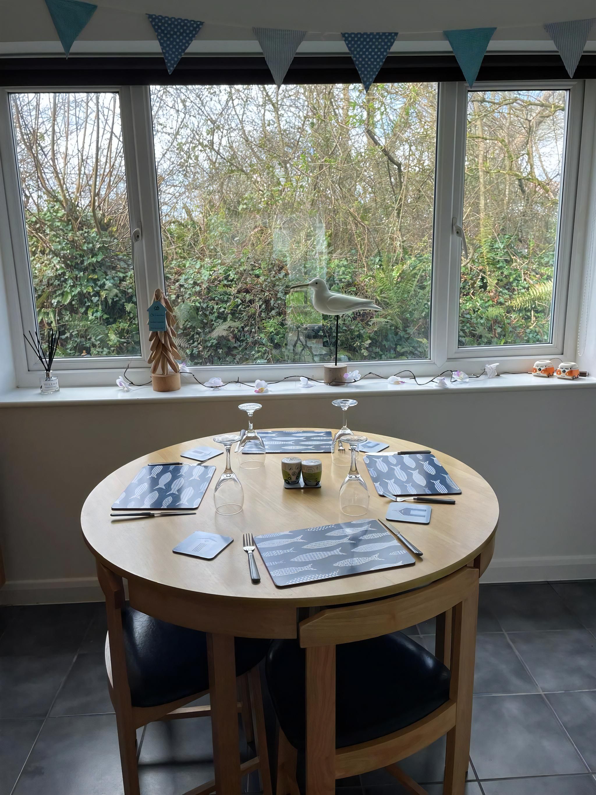 A round dining table with placemats, cutlery, and wine glasses set for four.