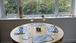 A round dining table with placemats, cutlery, and wine glasses set for four. - Atlantic Reach Cosy 2-bed With Parking (St. Columb Major)