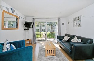 A living room with a blue sofa, a black sofa, a wooden coffee table, a TV mounted on the wall, and a large sliding glass door leading to an outdoor area.