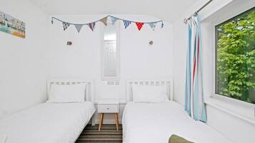 A twin room with two beds, a window with curtains, a small bedside table, and a wall-mounted light.
