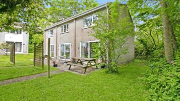 A two-story house with a patio, a wooden bench, and a small garden area.