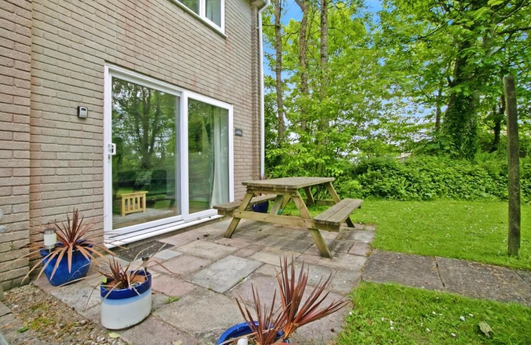 A brick house with a sliding glass door, a wooden picnic table, and potted plants.