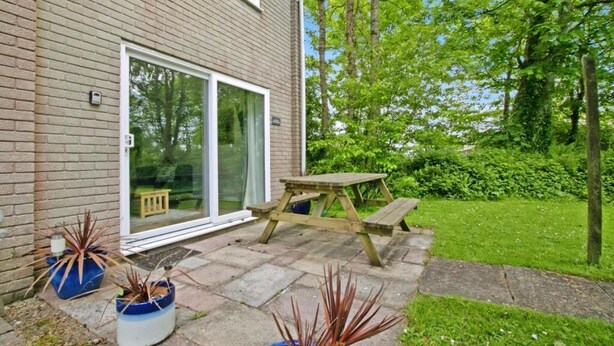 A brick house with a sliding glass door, a wooden picnic table, and potted plants. - Atlantic Reach Cosy 2-bed With Parking (St. Columb Major)
