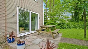 A brick house with a sliding glass door, a wooden picnic table, and potted plants.