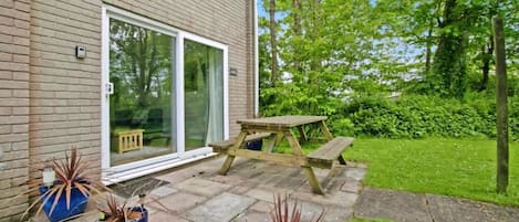 A brick house with a sliding glass door, a wooden picnic table, and potted plants.