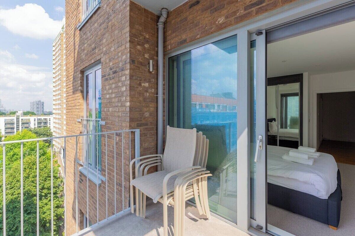 A balcony with a chair, a bed, and a sliding glass door to a bedroom.