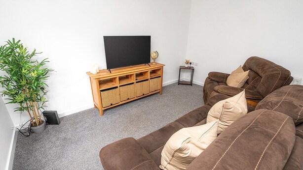 A living room with a brown sofa, a wooden entertainment unit, a potted plant, and a television.