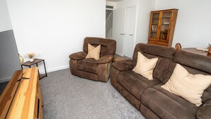 A living room with a brown leather sofa, a brown leather armchair, and a wooden coffee table. There is a wooden cabinet with glass doors in the background.
