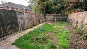 A backyard with a wooden fence, a concrete path, and a grassy area.