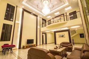 Un vaste salon doté d’un haut plafond, d’un lustre, d’un téléviseur à écran plat et d’un escalier menant à un niveau supérieur.