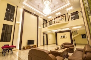 Uma sala de estar espaçosa com teto alto, um candelabro, uma TV de tela plana e uma escadaria que leva a um andar superior.