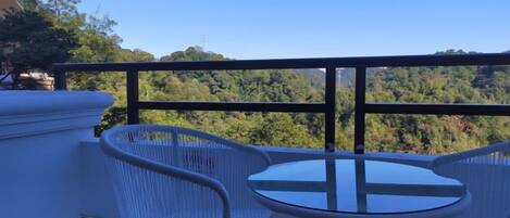 A balcony with a table and chairs, overlooking a forested landscape.