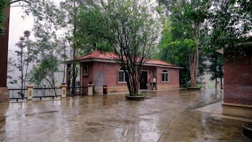 Un edificio de ladrillo con techo rojo, rodeado de árboles y suelo mojado, lo que indica lluvia reciente.