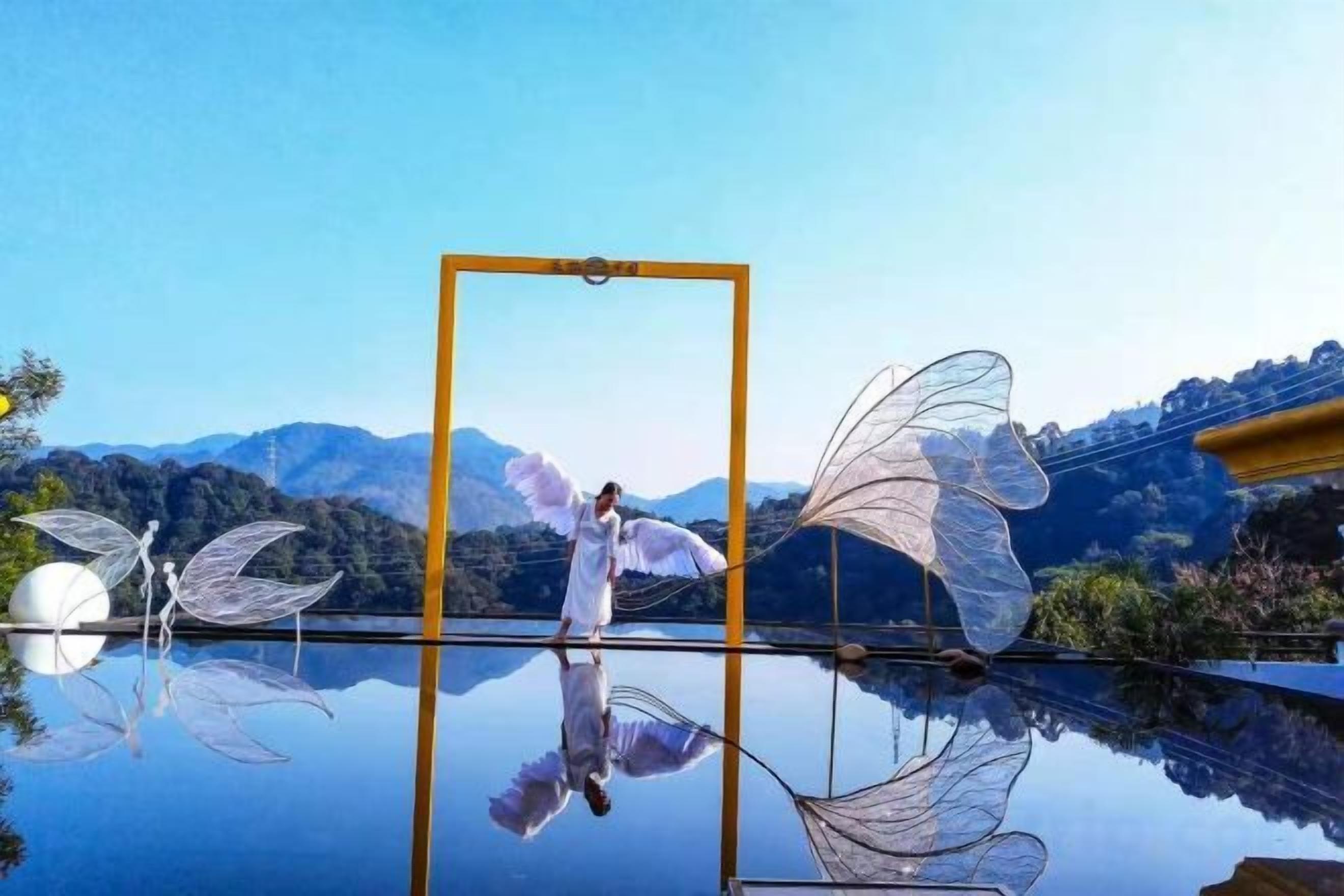 Superficie reflectante con una persona y alas, cielo despejado y montañas al fondo.