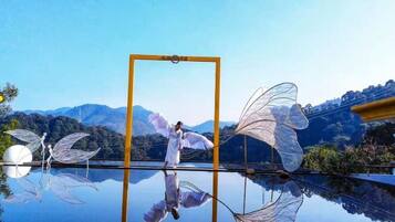 A reflective surface with a person and wings, a clear sky, and mountains in the background.