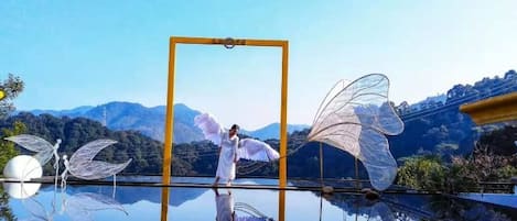 A reflective surface with a person and wings, a clear sky, and mountains in the background.