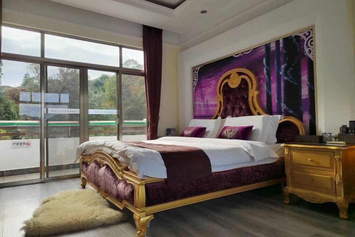 A bedroom with a large bed, a nightstand, a window with a view, and a wall tapestry.