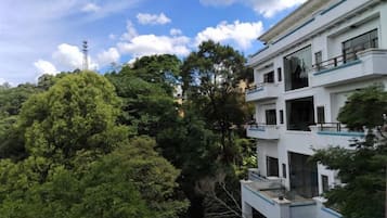 Un edificio de varios pisos con balcones y ventanas amplias, rodeado de abundante vegetación.