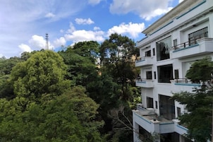Um edifício com várias andares, varandas e grandes janelas, cercado por vegetação densa.