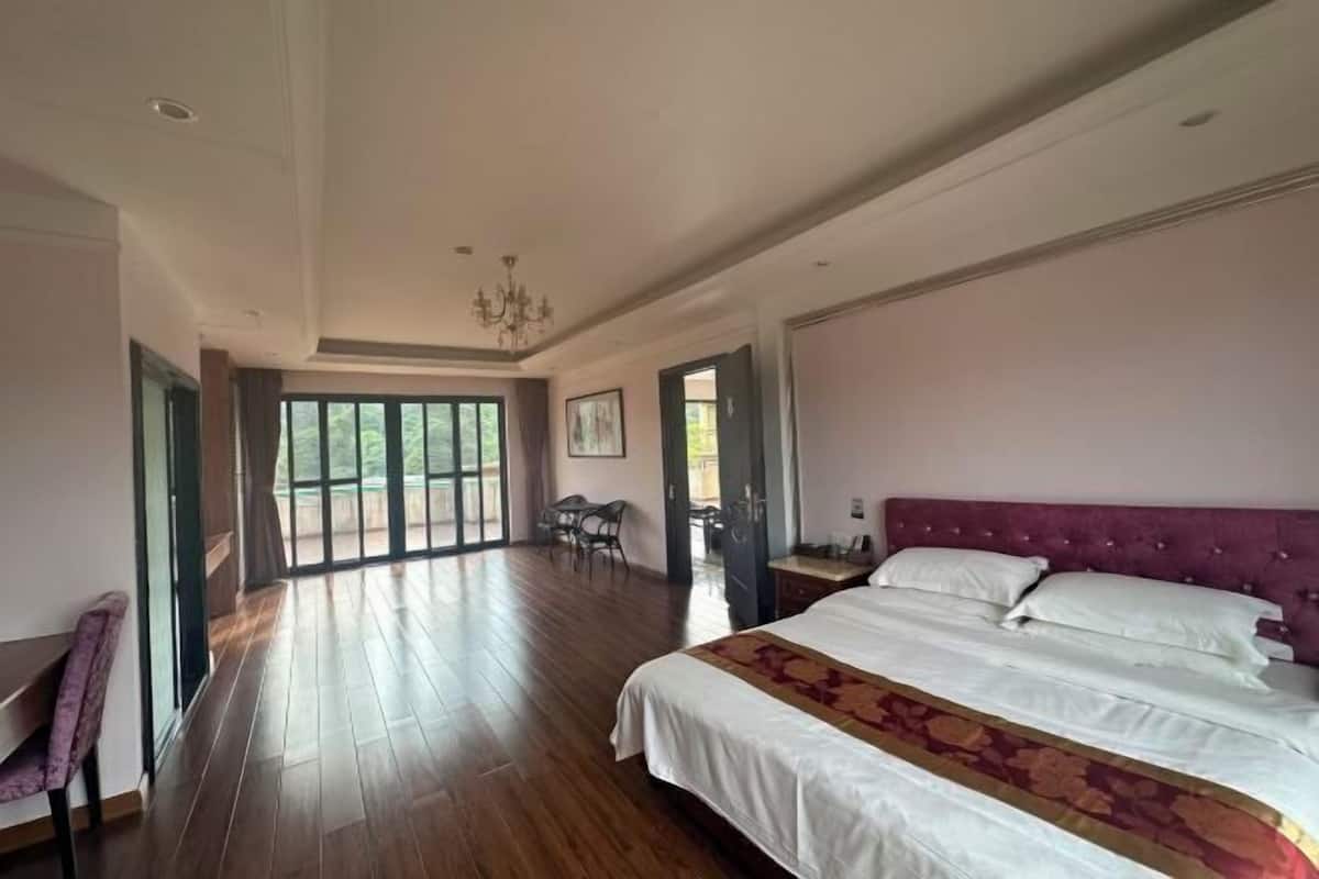 A spacious room with a large bed, a chandelier, and a view through a glass door to an outdoor area.