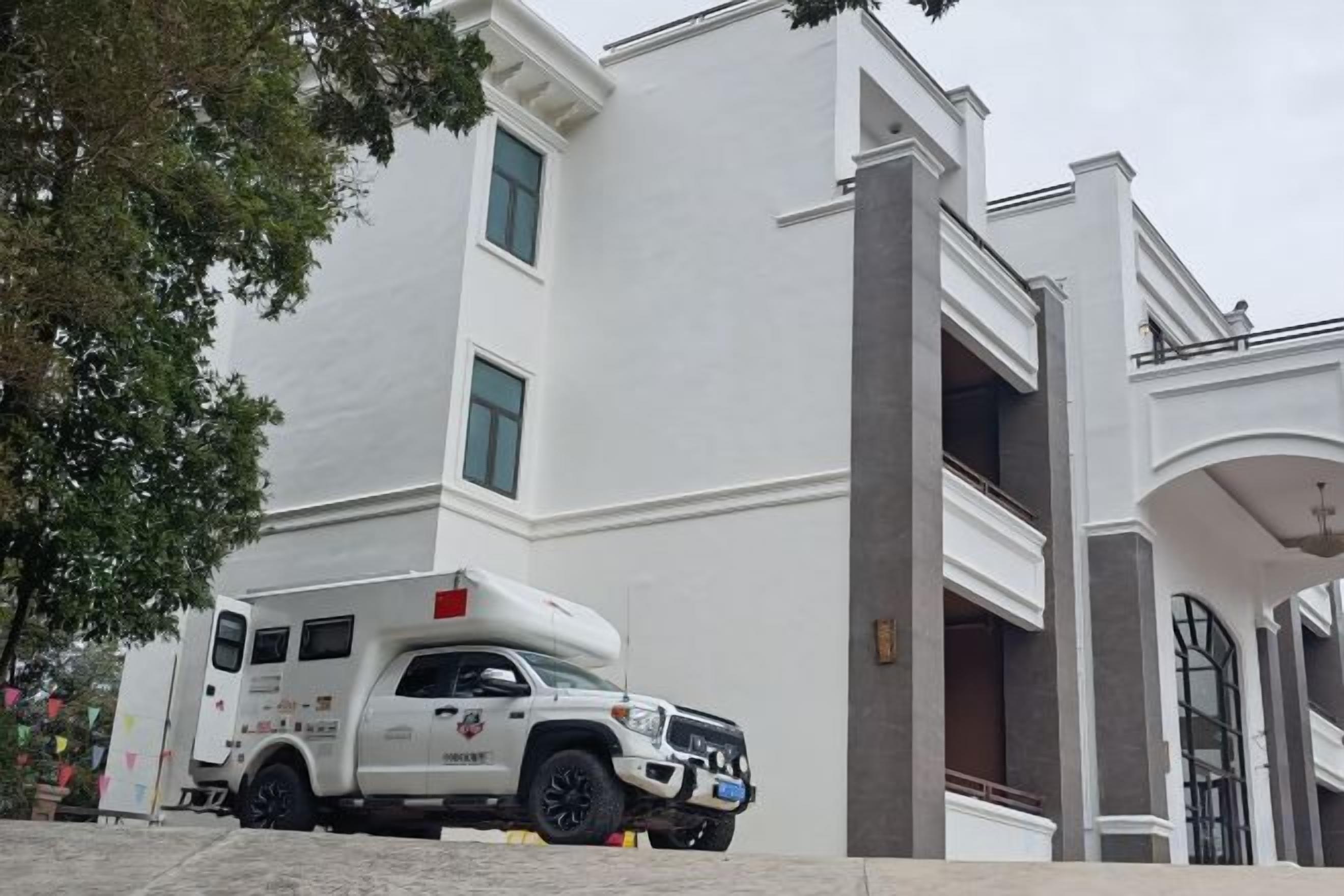 Un edificio blanco con una entrada amplia y una camioneta blanca estacionada adelante.