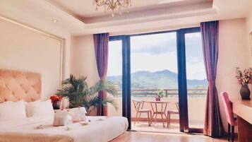 Un dormitorio con una cama grande, un candelabro, un balcón con mesa y sillas, y vistas a las montañas.