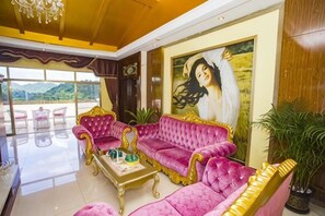 A room with a large pink sofa, a coffee table, and a painting on the wall. There are potted plants and a view of the outdoors. - Nankunshan Shihe Wonder Resort Villa (Longmen)